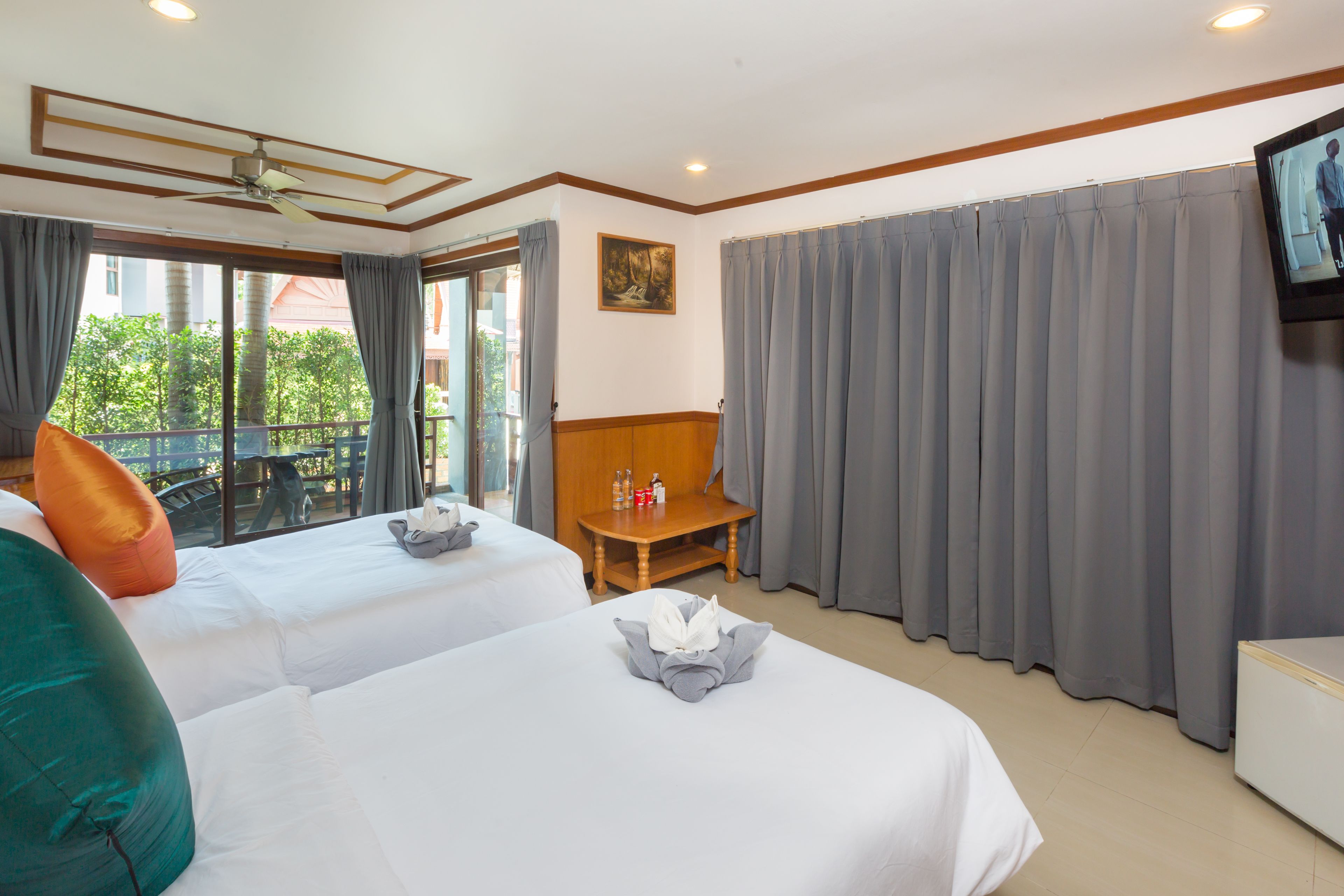 Een hotelkamer met twee bedden, een houten bankje, een televisie en een balkon met gordijnen.