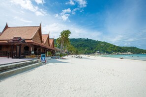 A beach with a traditional building with a tiled roof and a staircase leading to the beach. - Sunrise Resort (Ko Pha-ngan)