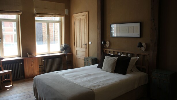 A bedroom with a large bed, a desk, a chair, a radiator, and a window with curtains. - 1669 Bed & Breakfast (Bruges)