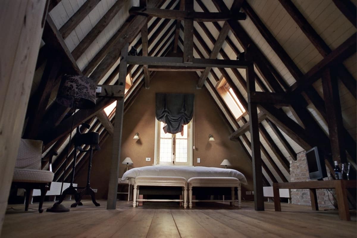 Une chambre mansardée avec un plafond haut, un grand lit, deux tables de chevet et une fenêtre avec des rideaux.