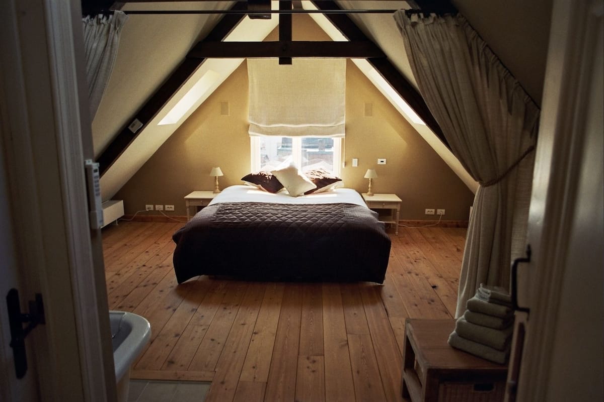 Une chambre avec un plafond en pente, un lit, deux tables de chevet et une fenêtre.