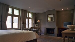 A hotel room with a large bed, a fireplace, a television, and a dining table. - 1669 Bed & Breakfast (Bruges)