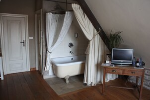 A bathroom with a bathtub, a wooden desk with a television, and a potted plant.