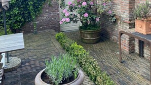 A courtyard with a brick wall, a tiled roof, and a potted plant with pink flowers. - 1669 Bed & Breakfast (Bruges)