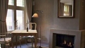 A room with a fireplace, a dining table with chairs, a floor lamp, and large windows with curtains. - 1669 Bed & Breakfast (Bruges)