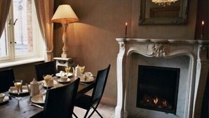 A dining area with a fireplace, a table set for two, and a lamp. - 1669 Bed & Breakfast (Bruges)