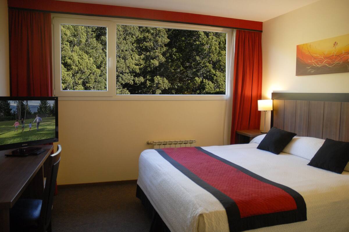 Ein Hotelzimmer mit Bett, Fernseher, einem Fenster mit Vorhängen und einem Bild an der Wand.