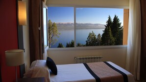 A hotel room with a large window offering a view of a lake and mountains.