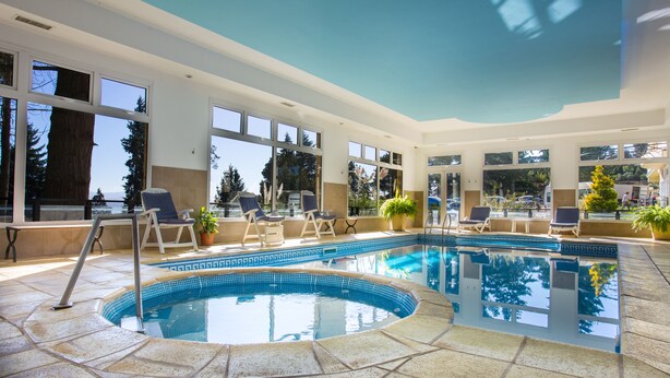 An indoor swimming pool with clear views of the outdoors, surrounded by lounge chairs and potted plants.