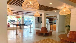 A spacious lobby with a central round table, multiple hanging wicker lamps, and a reception desk.