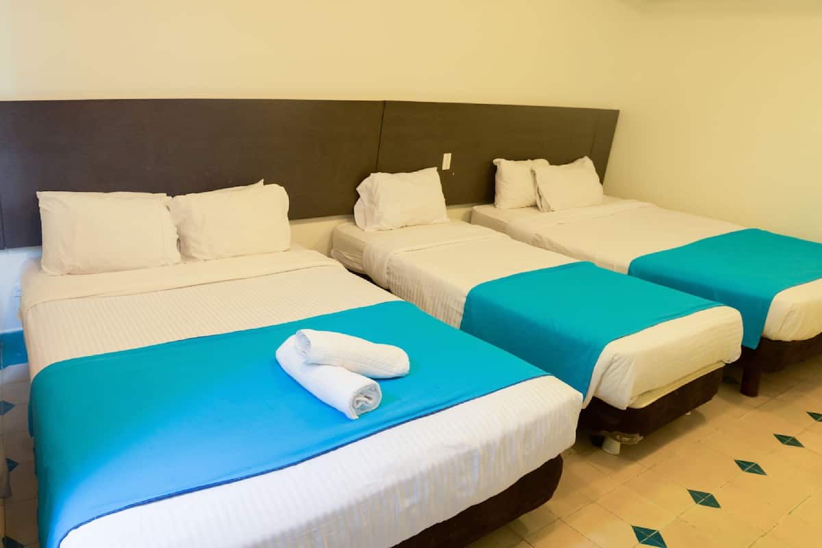 A hotel room with three beds, each with white bedding and a blue accent.