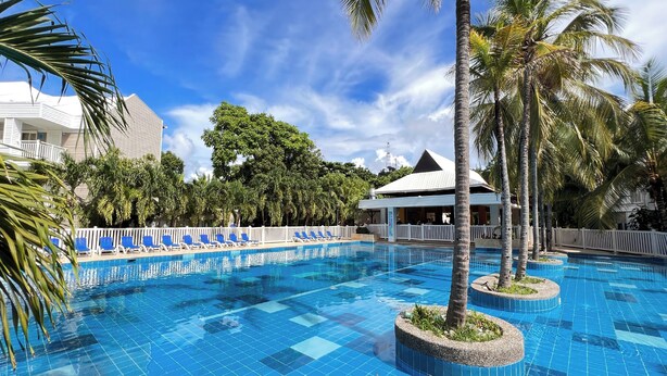 A swimming pool with blue tiles, surrounded by palm trees and lounge chairs.