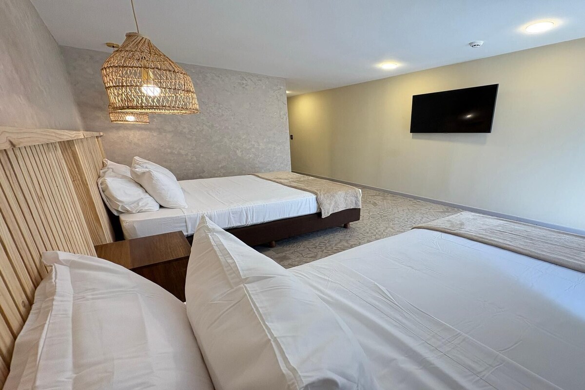 Camera d'albergo con due letti, una televisione a muro e un lampadario.