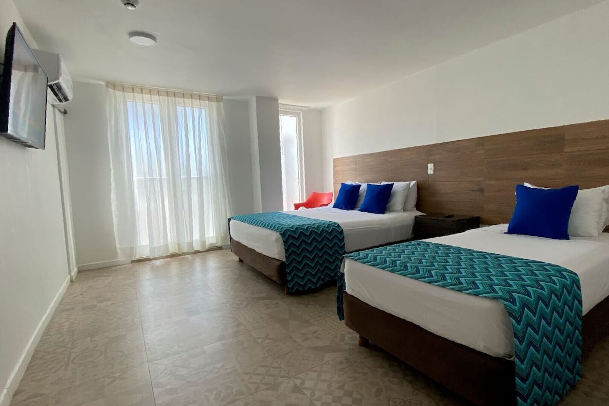 A hotel room with two beds, a TV, and a window with curtains.