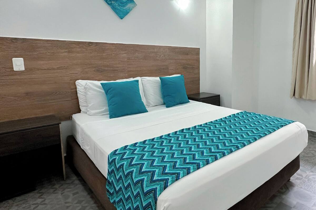 A neatly made bed with a patterned blanket, a wooden headboard, and a nightstand with a lamp.