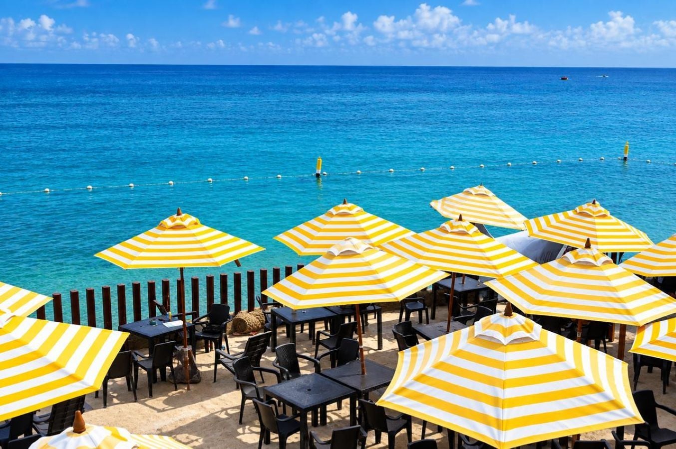 Ein Café direkt am Strand mit Außenplätzen und Sonnenschirmen, mit Blick auf das klare, blaue Meer.
