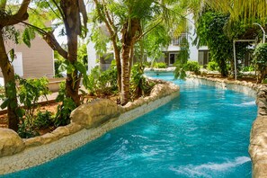 Une piscine bordée de pierres, entourée d’une végétation luxuriante et d’arbres.
