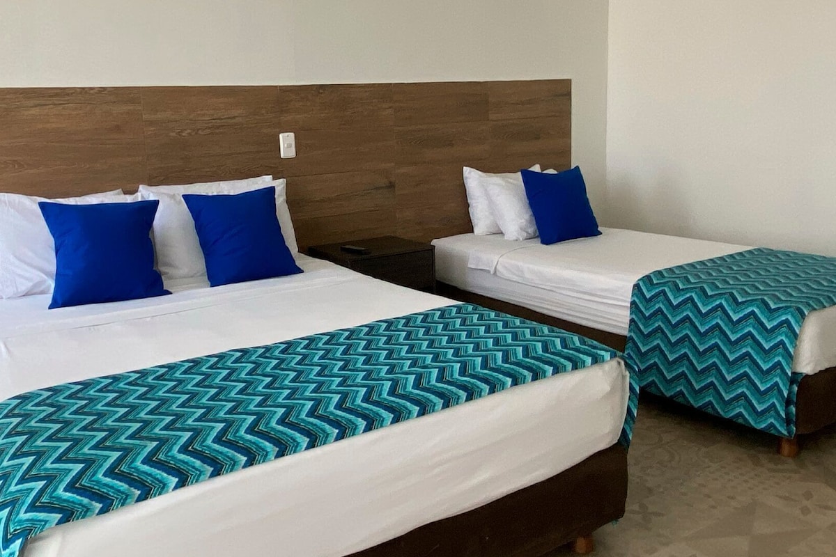 Deux lits jumeaux avec du linge de lit blanc et des oreillers bleus, une tête de lit en bois et une couvre-lit à motifs.