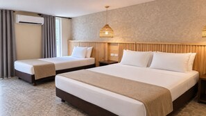 Une chambre d’hôtel avec deux lits, une tête de lit en bois, un climatiseur fixé au mur et un luminaire suspendu.
