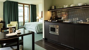 Una camera d'albergo con un letto, un tavolo da pranzo con sedie, un angolo cottura con forno a microonde e vista sulla città.