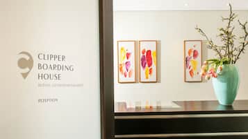 Un área de recepción con el logotipo de 'Clipper Boarding House' y dos cuadros abstractos en la pared.