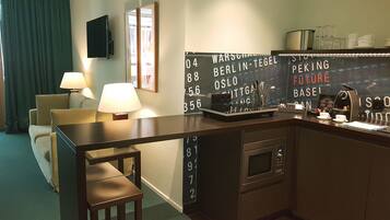 A hotel room with a kitchenette, a sofa, two lamps, and a wall with numbered windows.