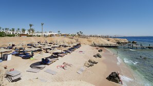 Uma praia com fileiras de espreguiçadeiras e guarda-sóis, um litoral rochoso e águas azul-claras.