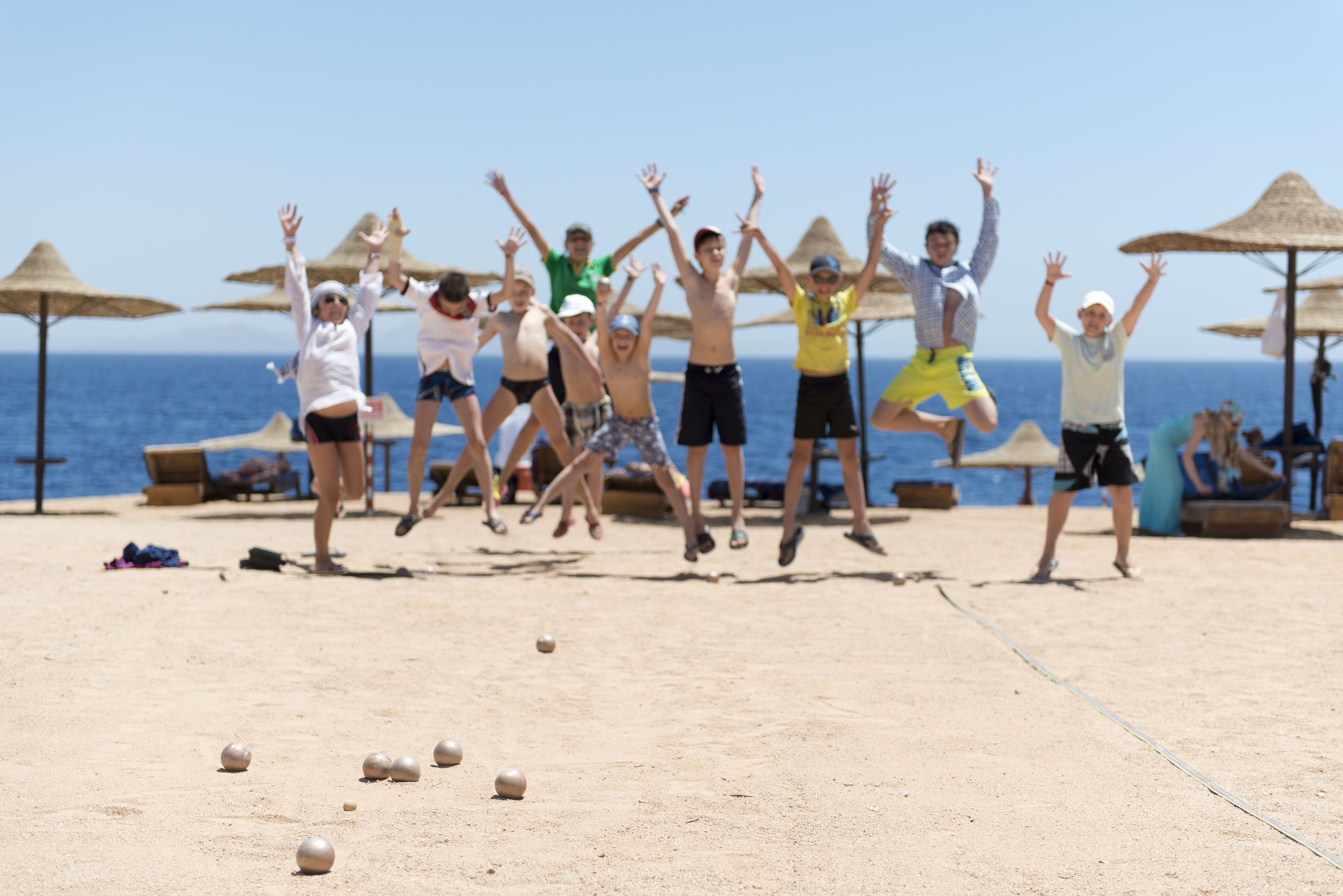 Un groupe de personnes joue à un jeu de balle sur une plage de sable, avec des parasols et l’océan en arrière-plan.