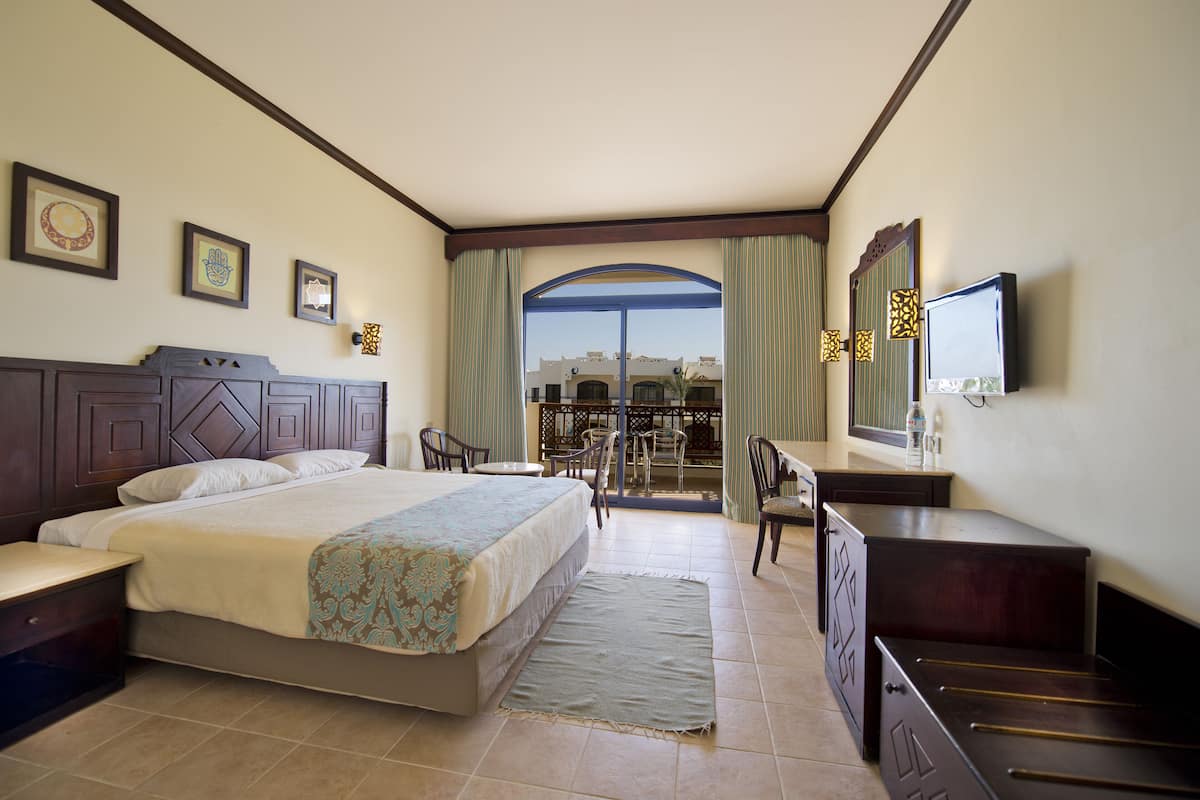 A hotel room with a bed, desk, chairs, and a TV.