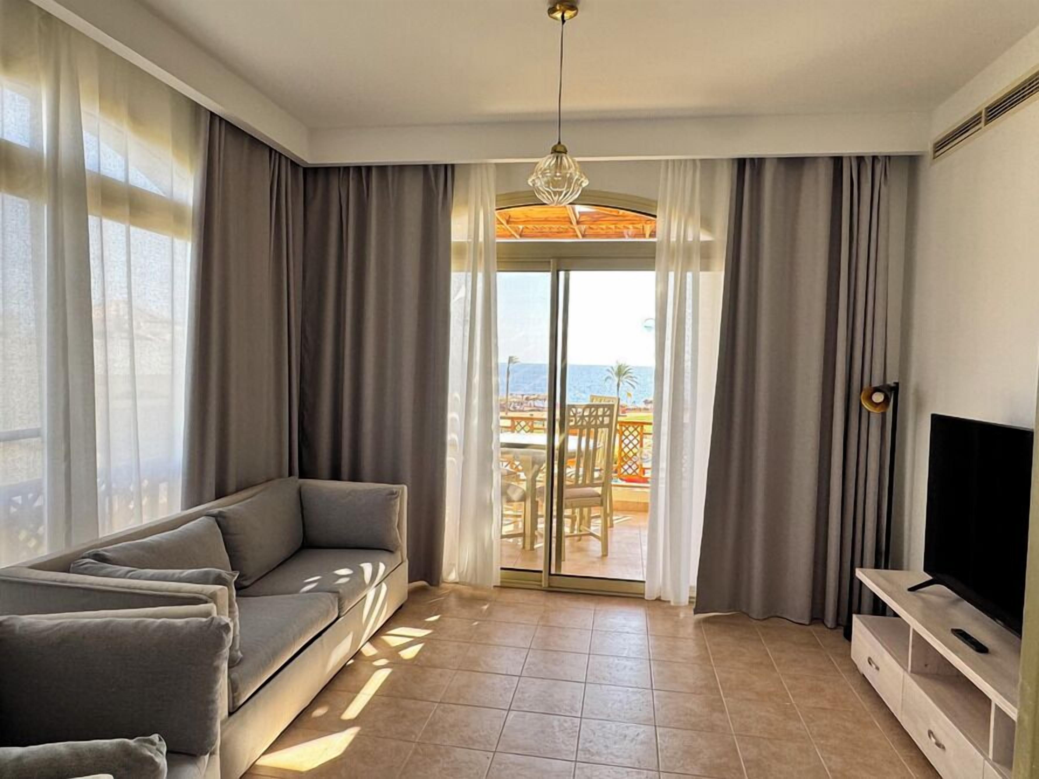 A living room with a sofa, TV, and a view of the sea through a glass door.