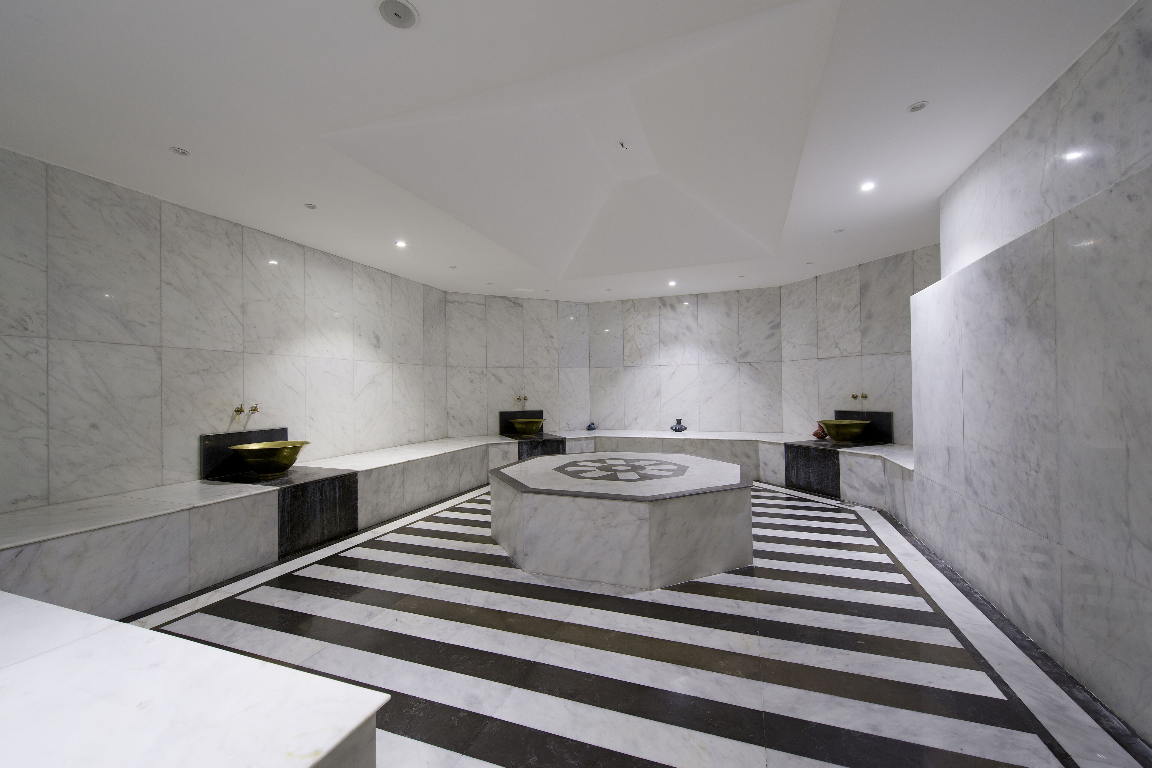 A modern bathroom with a central circular sink, black and white striped floor, and marble walls.