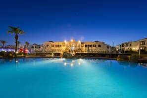 Un hôtel doté d’une piscine, de palmiers et offrant une vue sur le ciel nocturne.