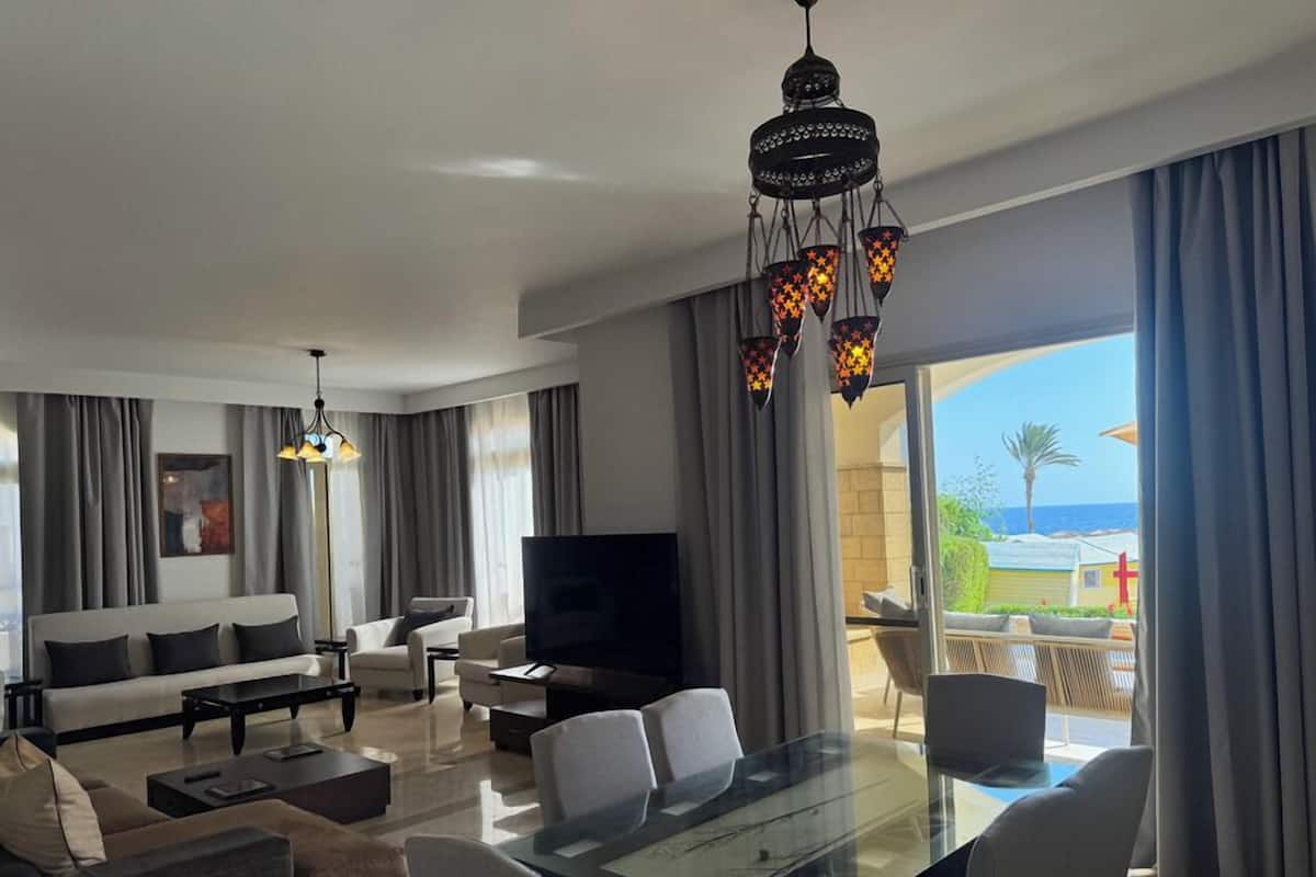 A modern living room with a sofa, coffee table, TV, and a dining area with chairs and a glass table.