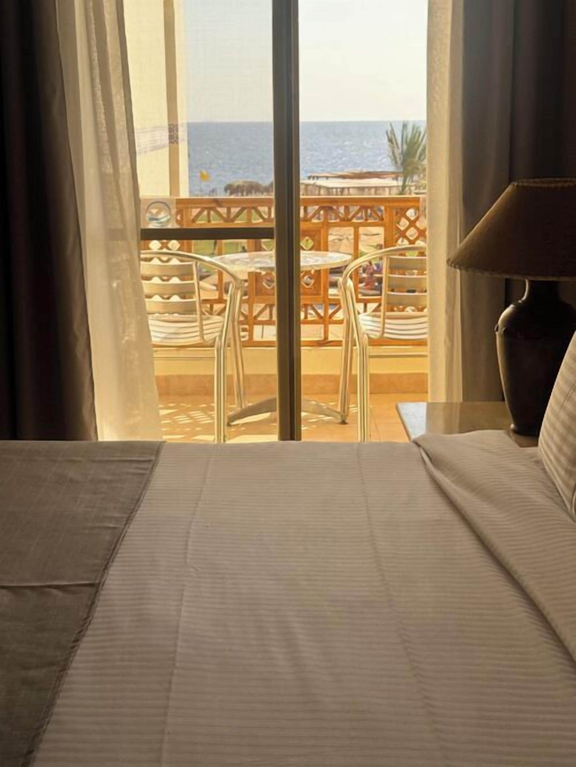 Quarto de hotel com cama, mesa e cadeiras numa varanda com vista para o mar.