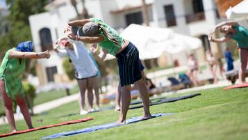 A group of people stretching on mats in an outdoor setting with buildings in the background.