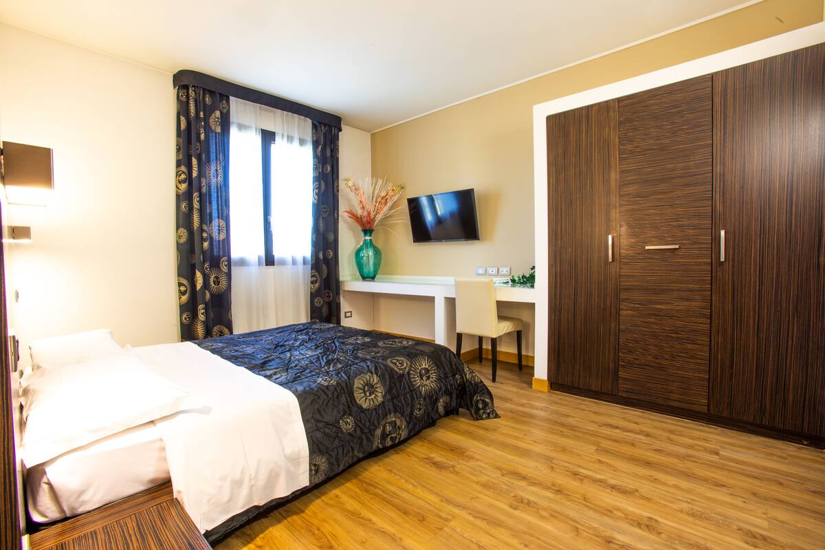 A hotel room with a bed, desk, TV, and wardrobe.