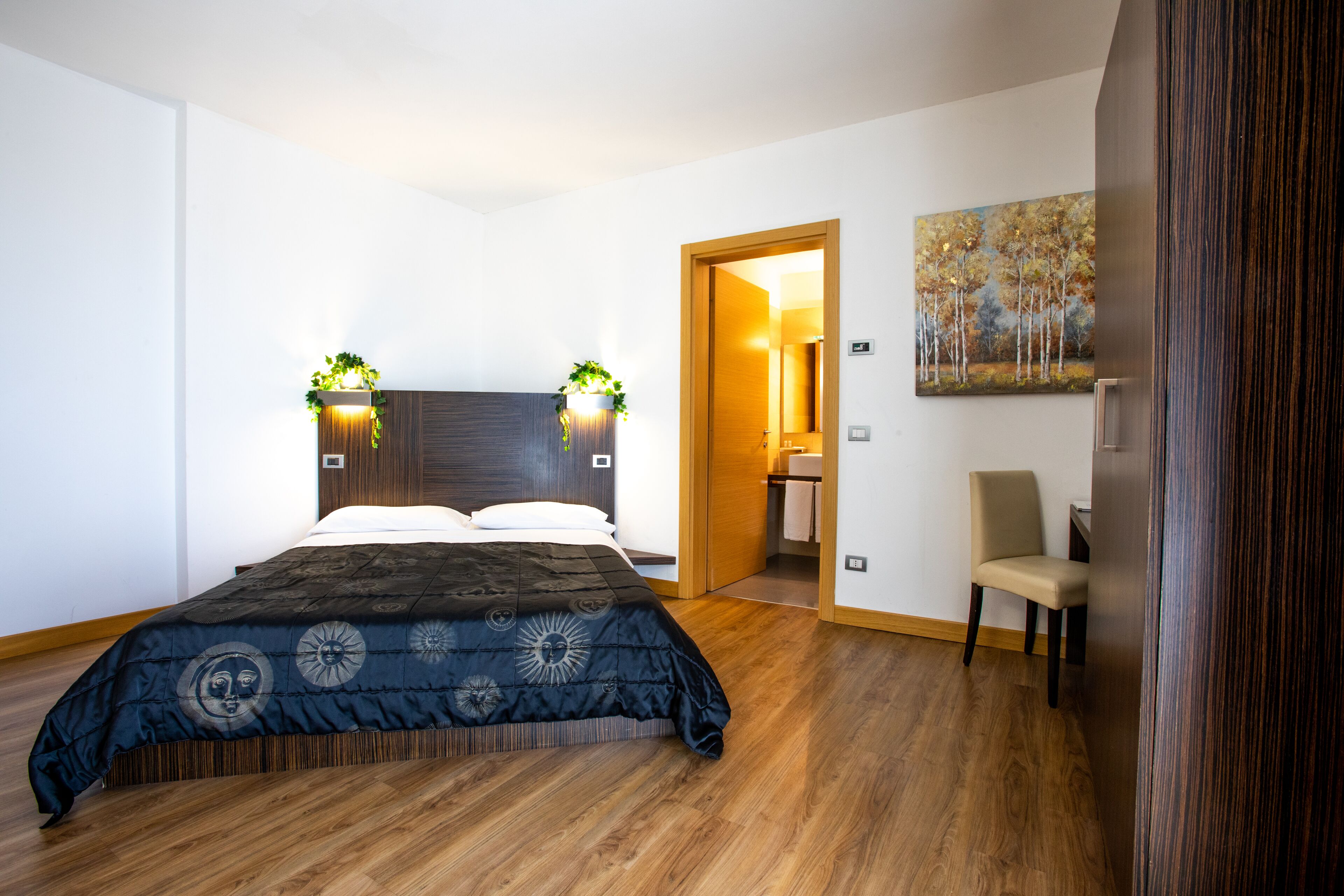 A modern bedroom with a large bed, wooden flooring, a chair, and a painting on the wall.