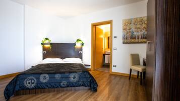 A modern bedroom with a large bed, wooden flooring, a chair, and a painting on the wall.