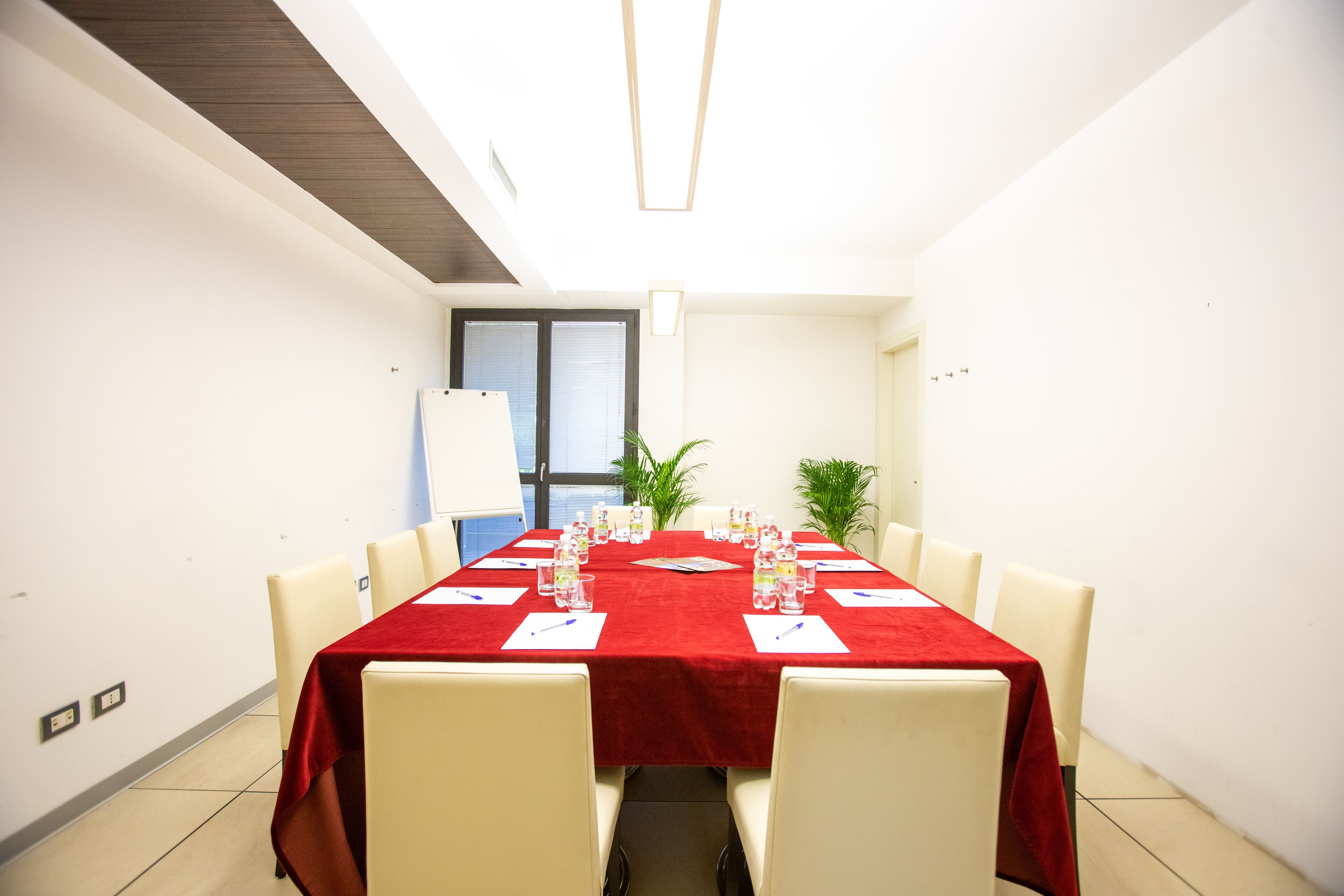 A conference room with a red tablecloth, white chairs, and a long table.