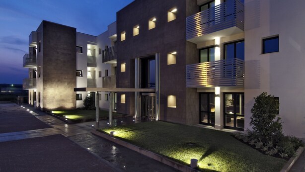 A modern multi-story building with balconies, illuminated windows, and a well-maintained lawn. - Matrix Hotel & Residence (Vigonza)