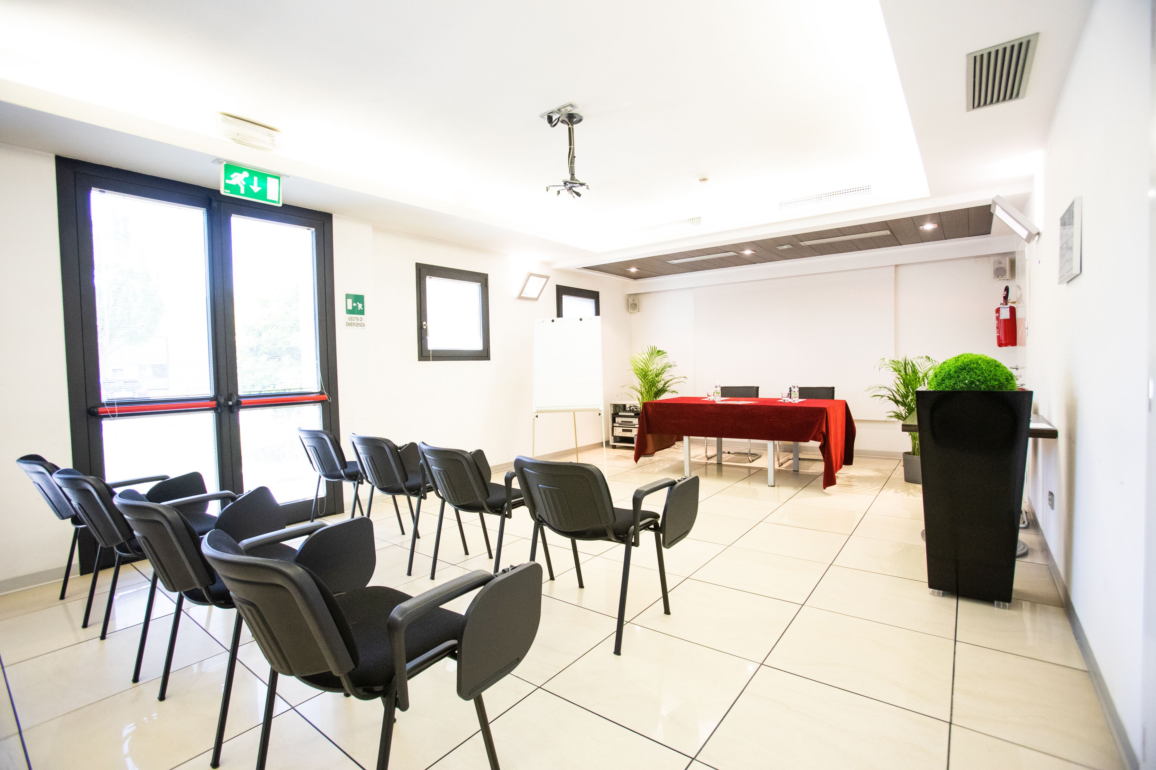 A conference room with chairs arranged in rows, a table with a red tablecloth, and a potted plant.