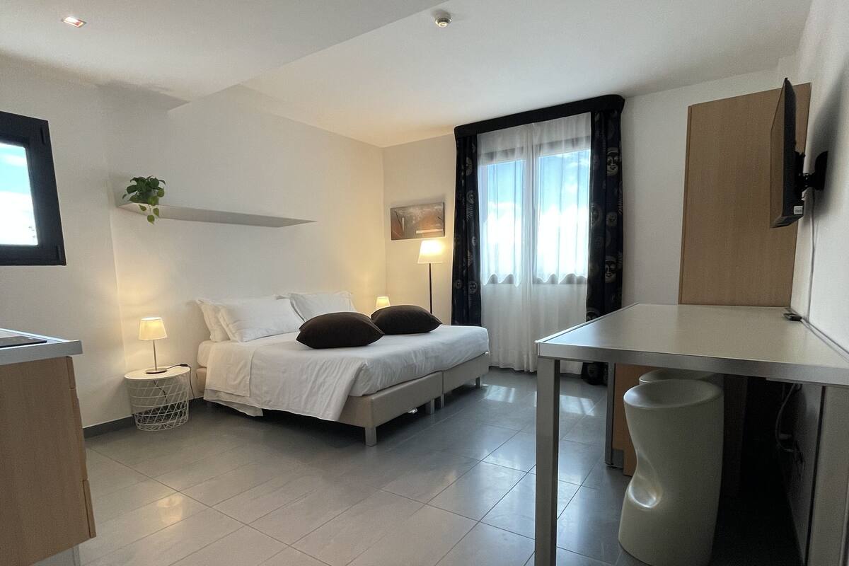 A modern bedroom with a bed, bedside tables, a desk, and a window with curtains.