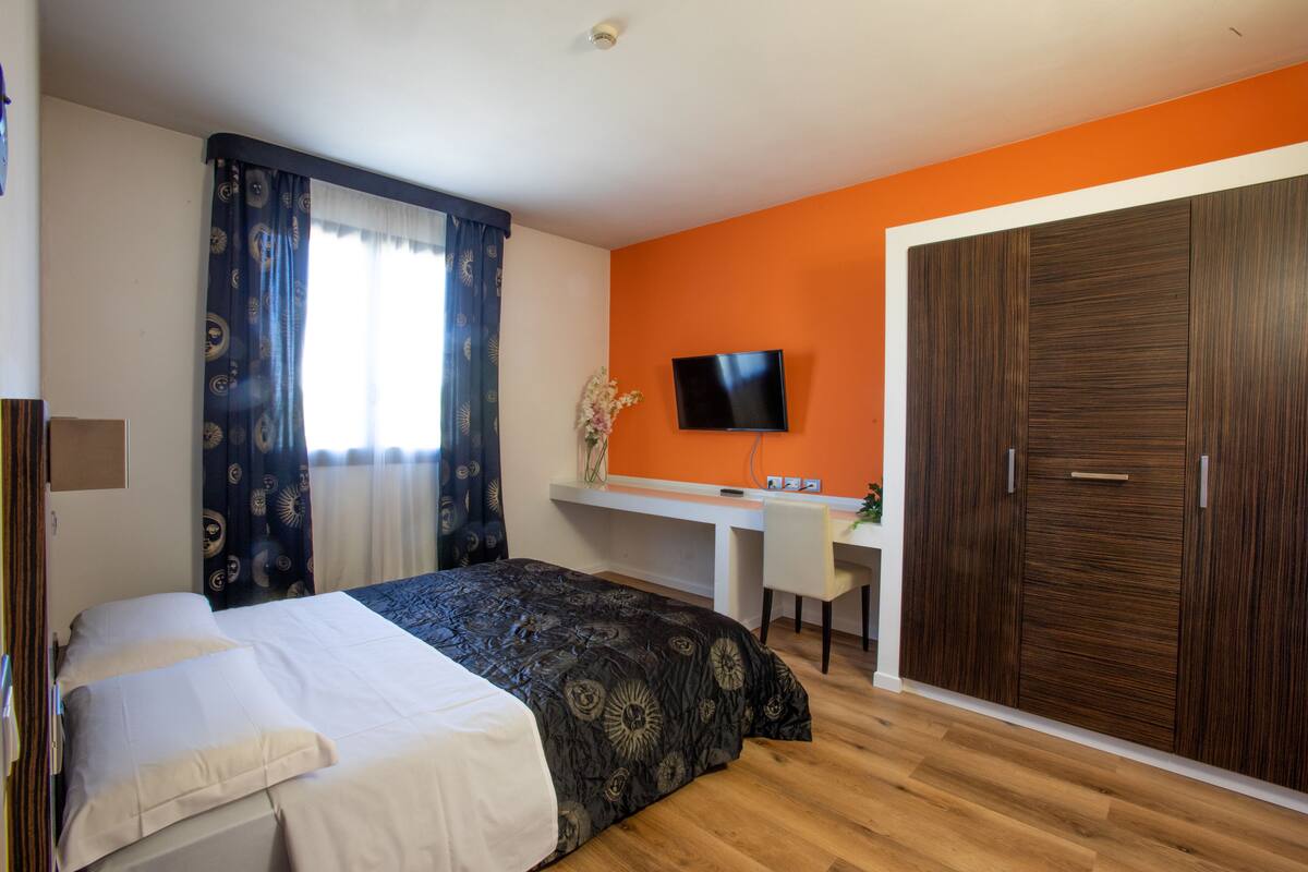 A bedroom with a bed, desk, TV, and wardrobe.