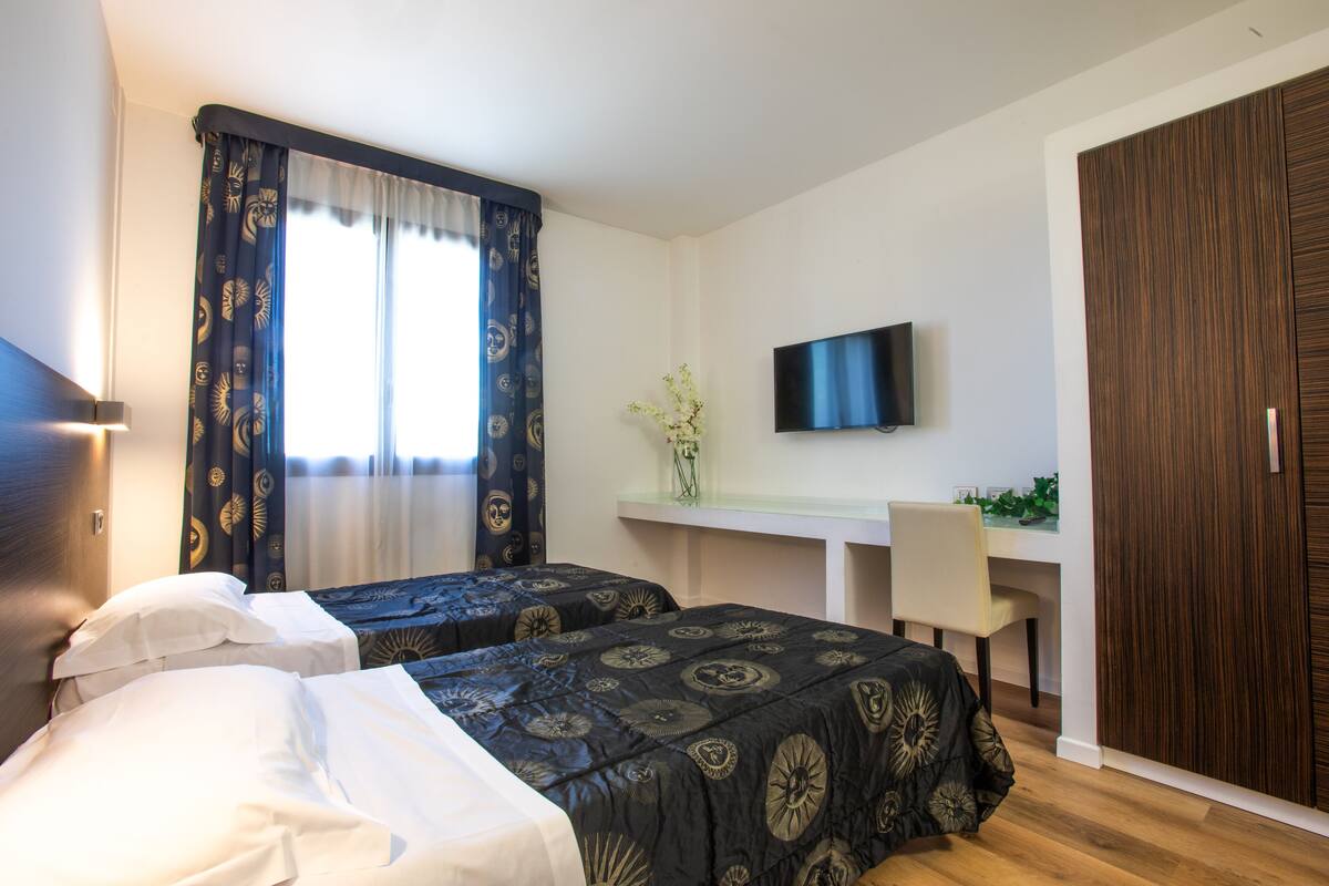 A hotel room with two beds, a desk with a chair, a TV, and a wardrobe.