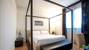 A modern bedroom with a four-poster bed, a bedside table with a vase of flowers, and a chair. - Matrix Hotel & Residence (Vigonza)