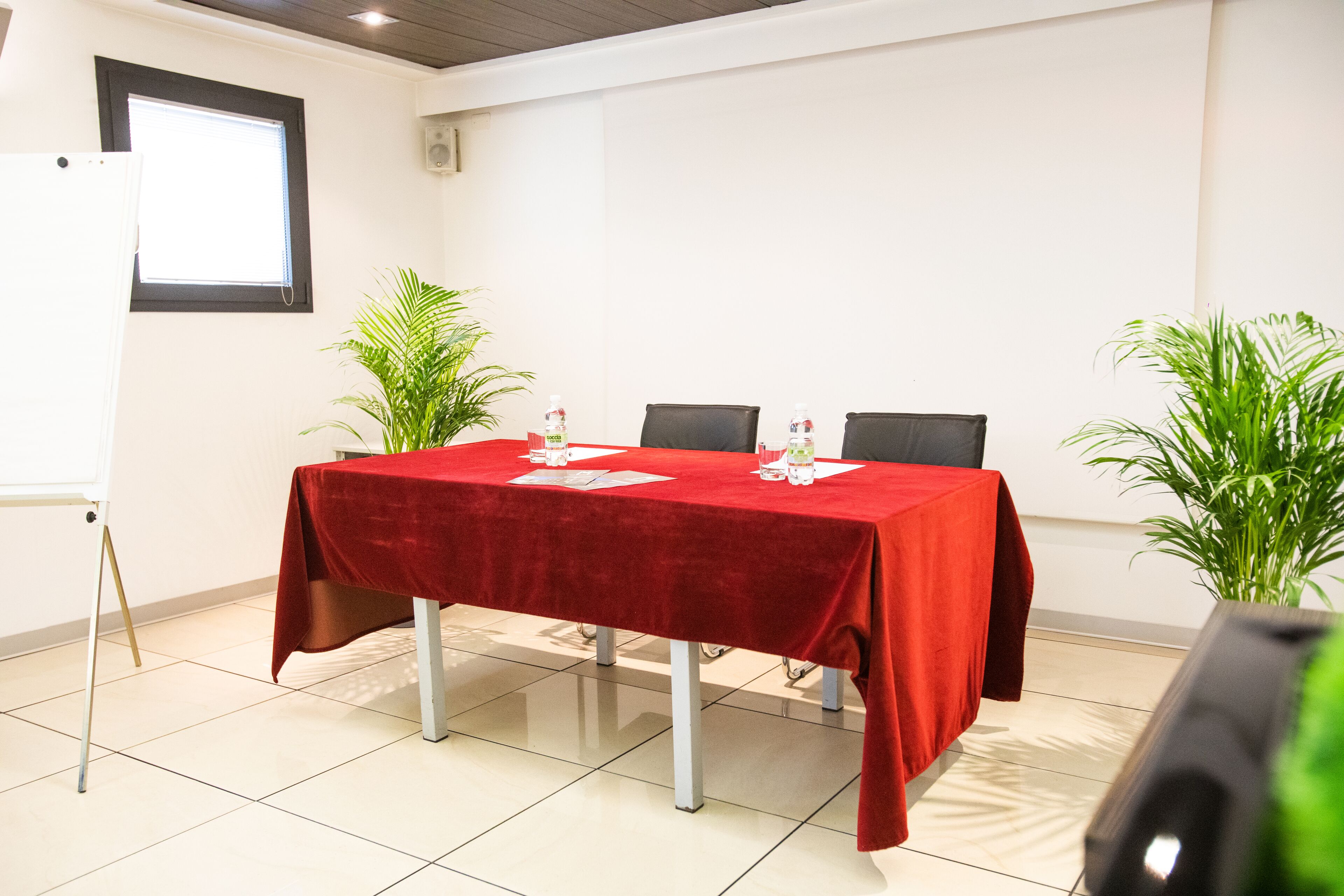 Une salle de conférence avec une table rouge, deux chaises et deux plantes en pot.