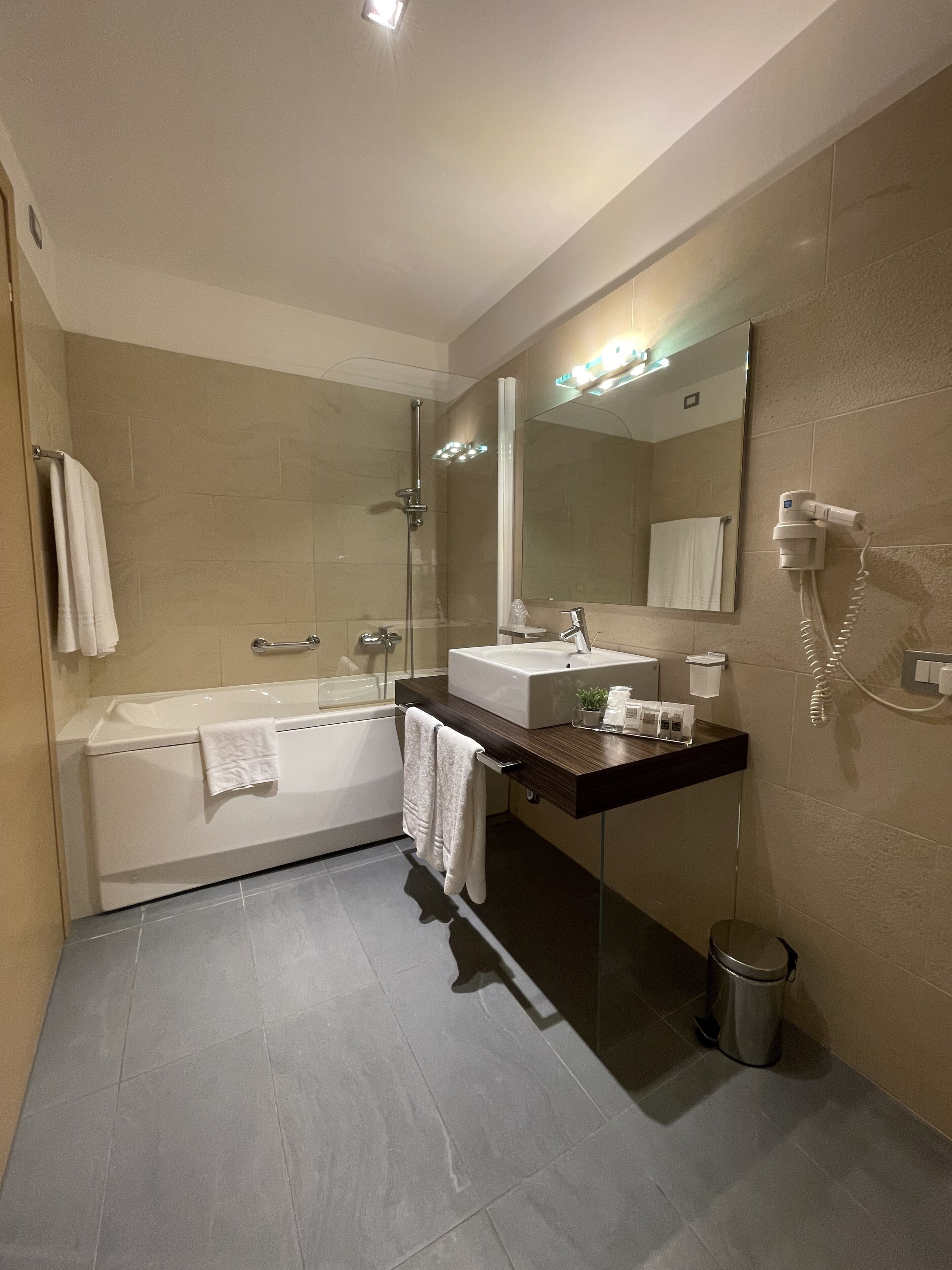 A modern bathroom with a bathtub, a sink, a mirror, and a hairdryer on the wall.