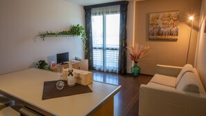 A modern living room with a sofa, a dining area with a table, a TV, and a large window with curtains. - Matrix Hotel & Residence (Vigonza)