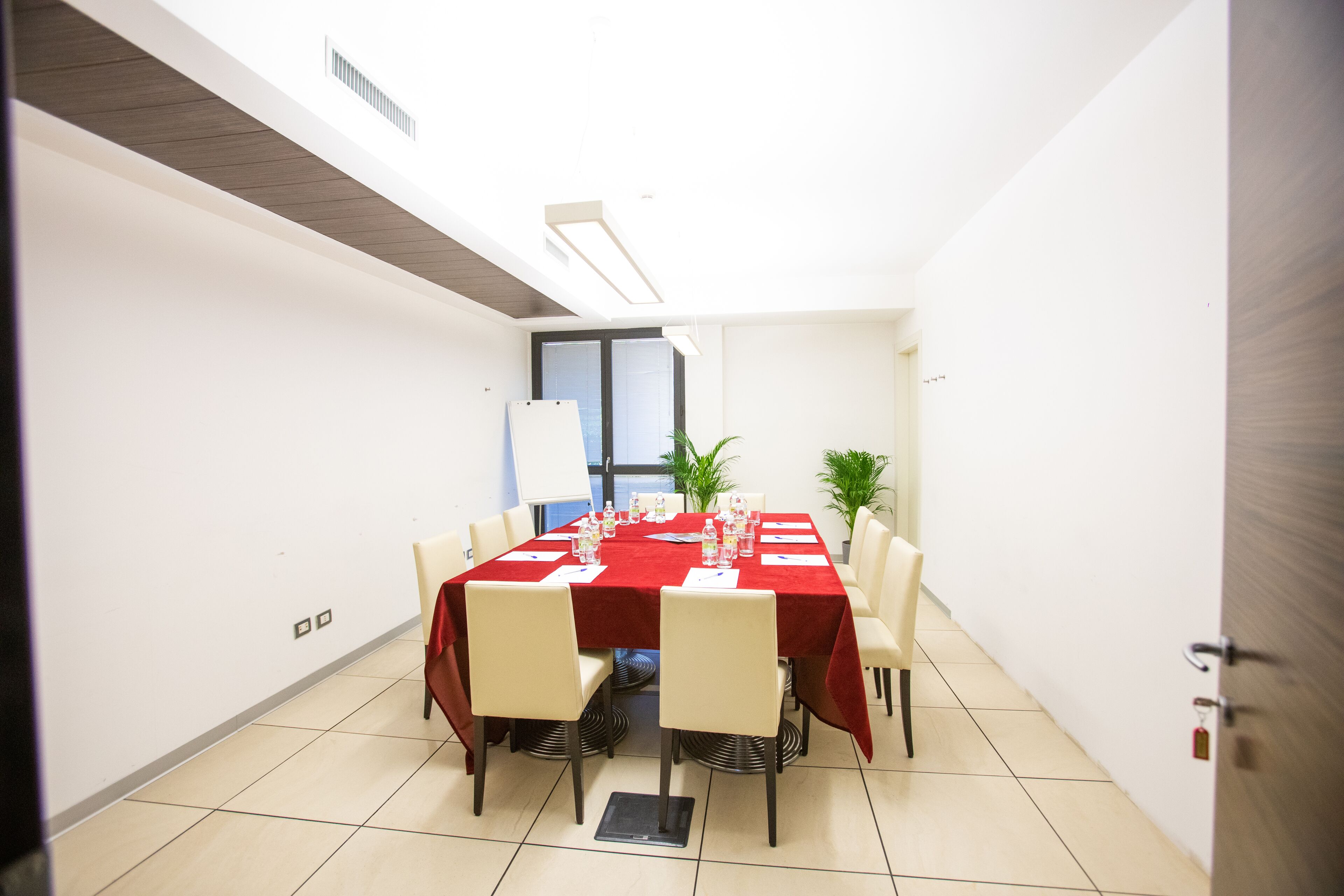 Un salón de conferencias con una mesa roja, sillas blancas y una pizarra.