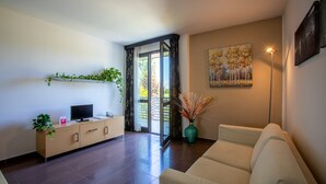 A modern living room with a sofa, a TV on a wooden cabinet, a vase with dried plants, and a painting on the wall. - Matrix Hotel & Residence (Vigonza)